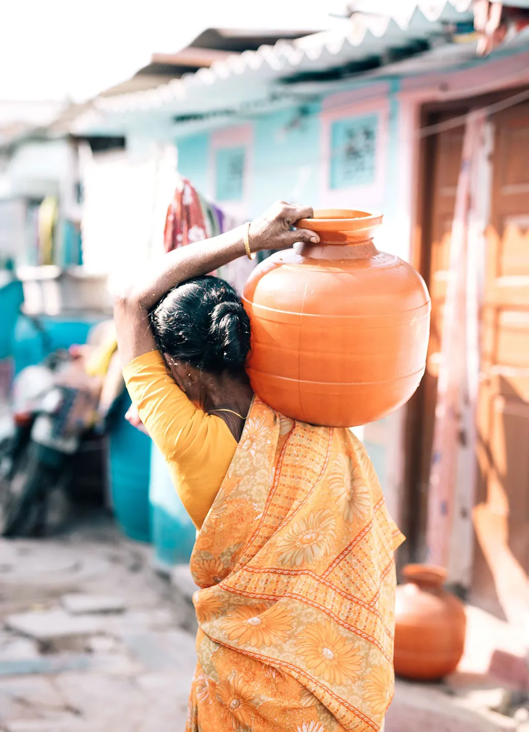 Woman walking down the street carrying an orange water vessel on her shoulder.