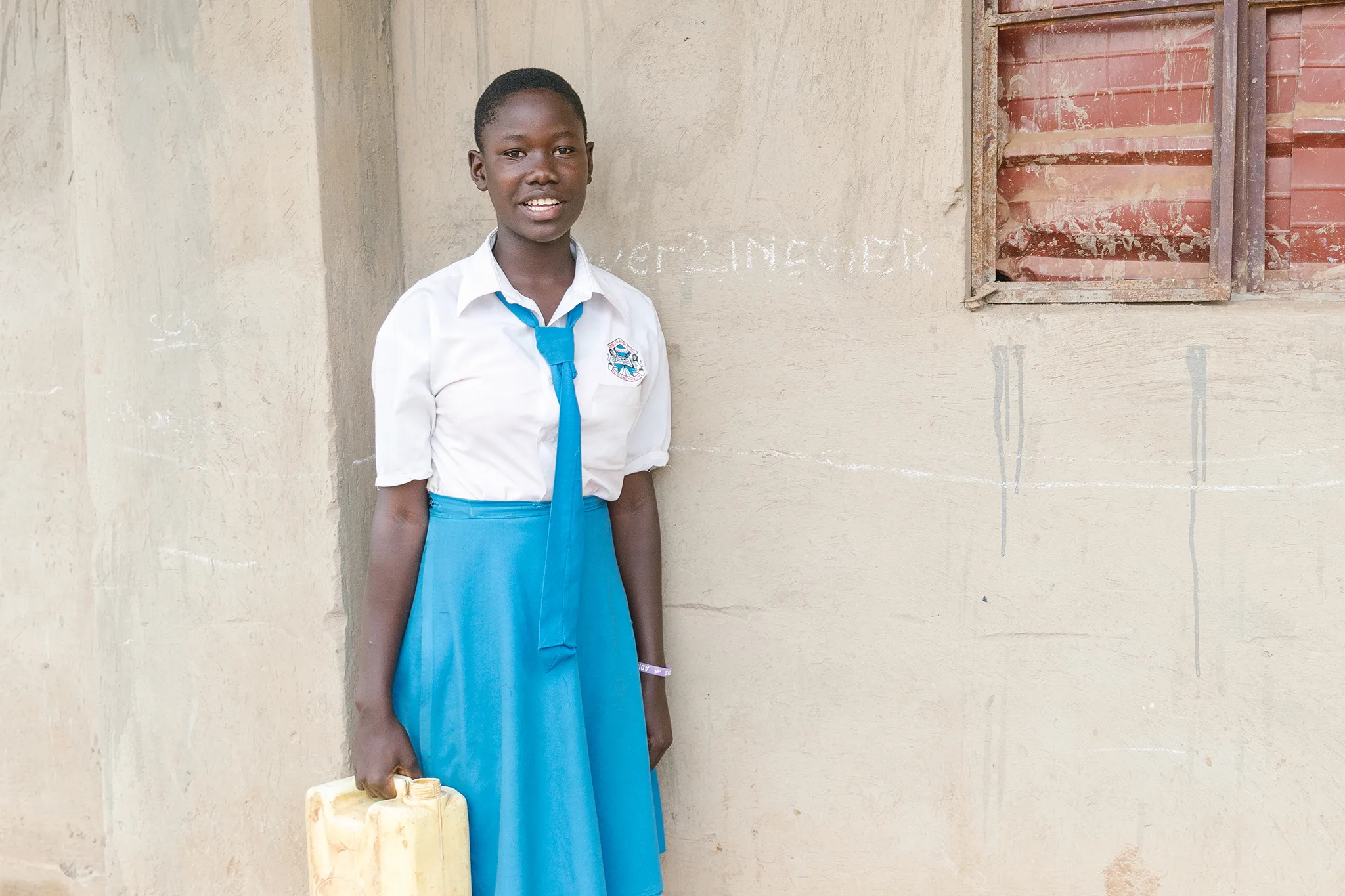 Young woman in her white and blue school uniform carrying a yellow water vessel.