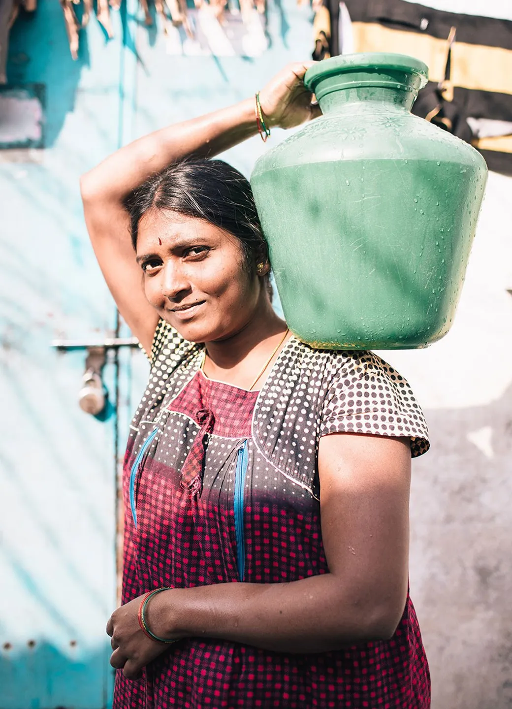 Woman carrying a teal water vessel on her left shoulder in Hyderabad, India.